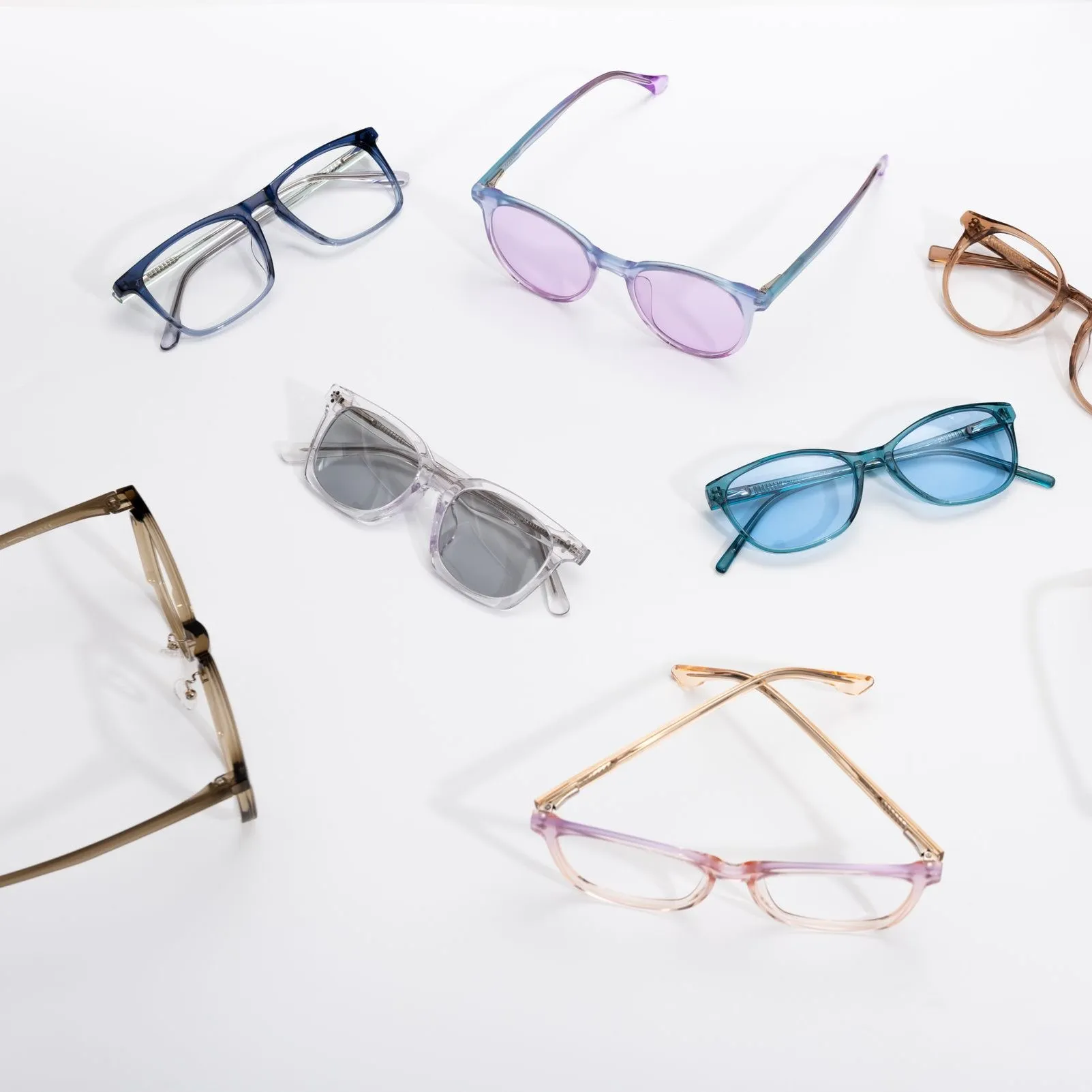 Varias monturas de colores y lentes tintados sobre una superficie blanca