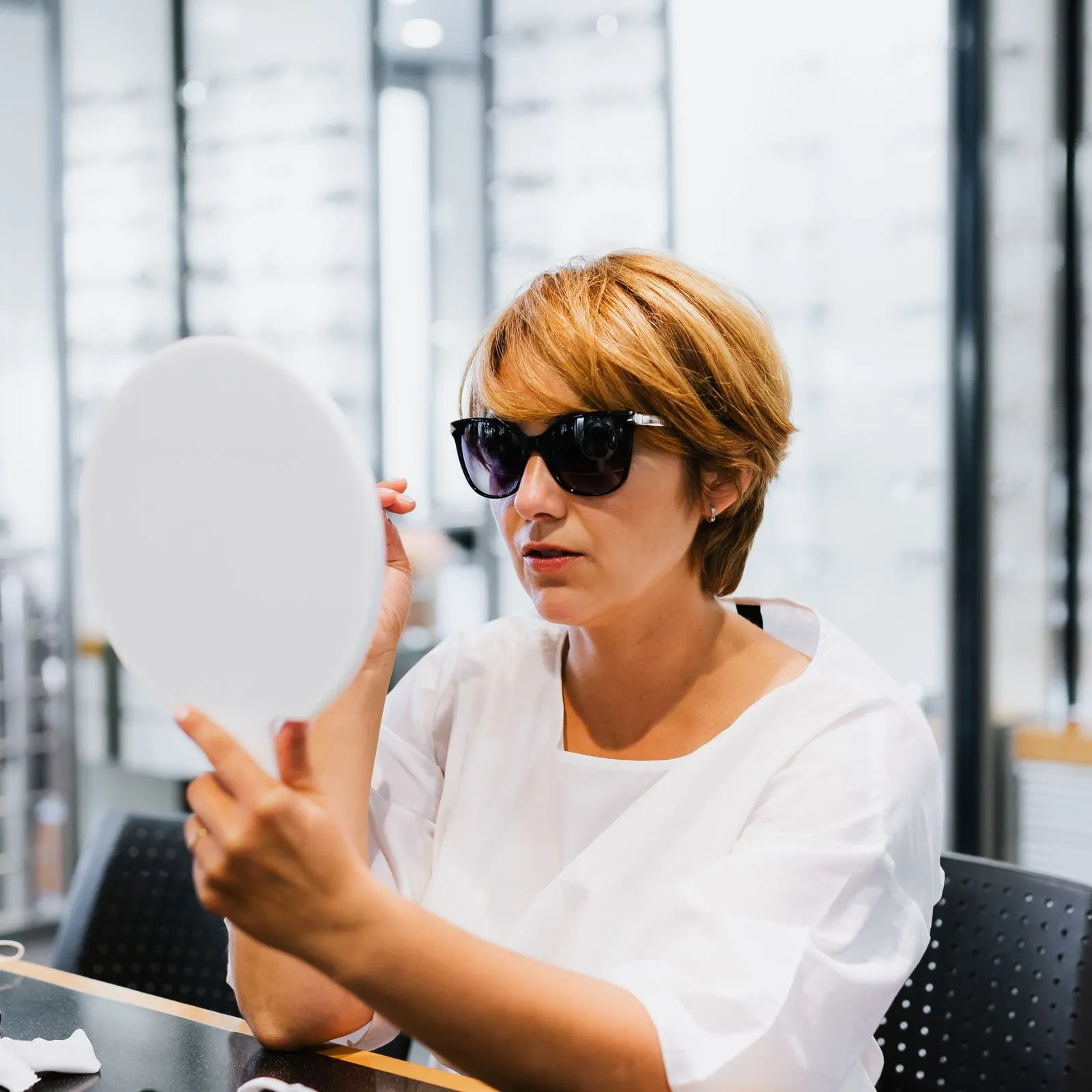 Clienta con gafas de sol mirándose en un espejo de mano dentro de una óptica