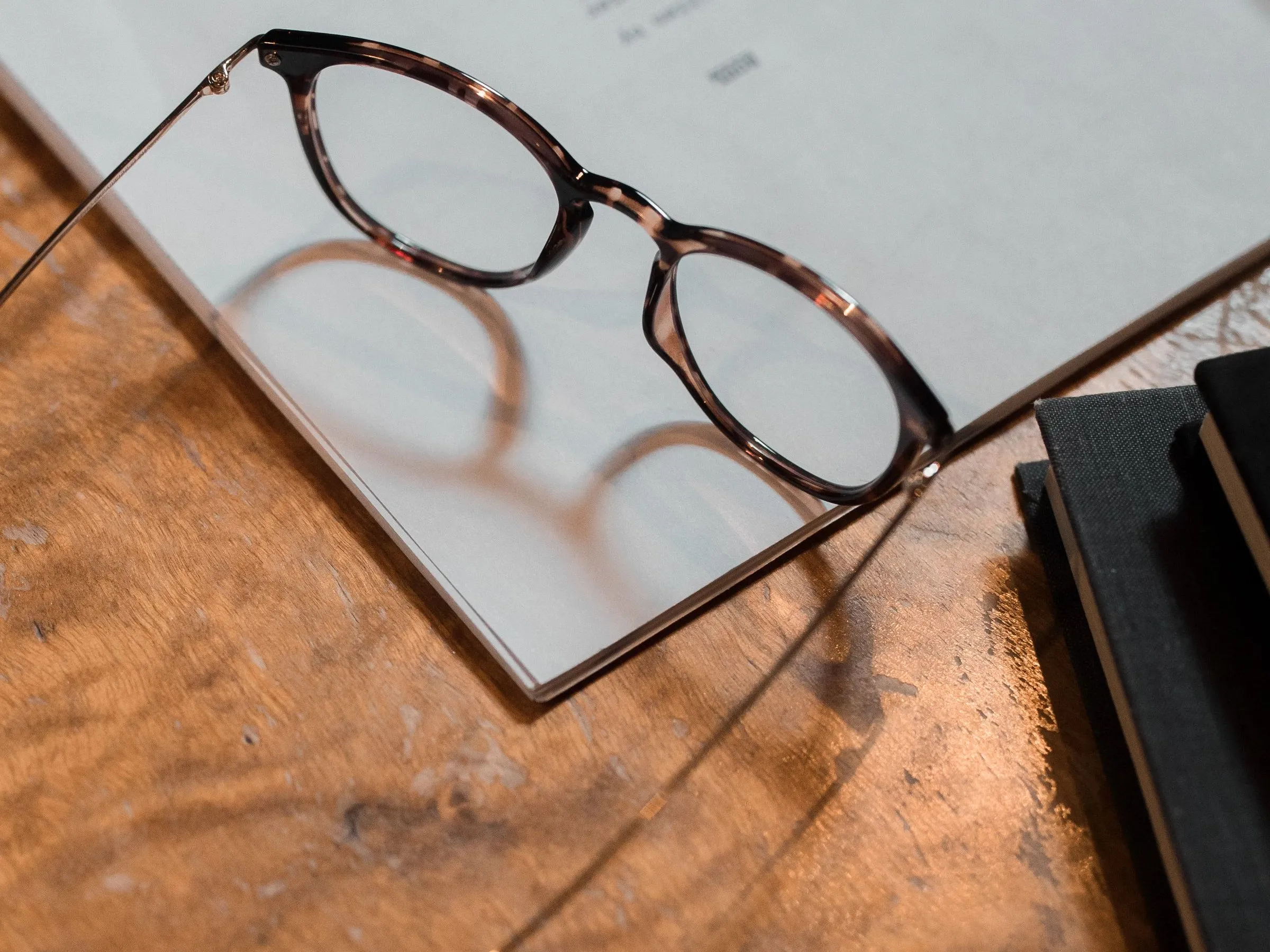Gafas de montura carey sobre una revista abierta en una mesa de madera